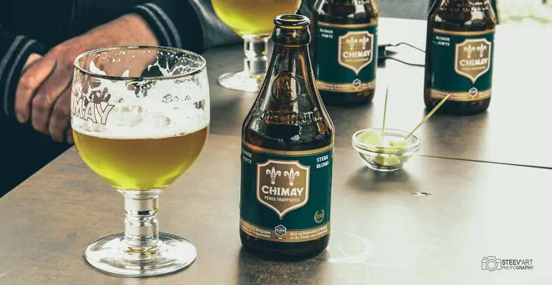Une Chimay Verte servie dans son verre, avec des cubes de fromage